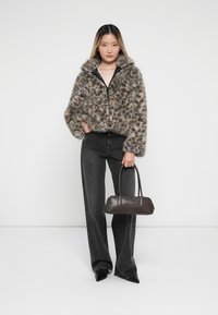 Faux fur cropped jas met een bruin en grijs leopardpatroon, ritssluiting, gecombineerd met zwarte high-waisted jeans en een donkerbruine handtas.