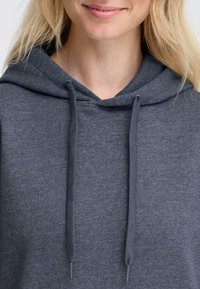 Pilkas džemperis su raišteliu, minkšta tekstūra ir atsipalaidavęs dizainas. Medžiaga yra lygi, tvirta mišri medžiaga, idealiai tinkanti kasdieniam dėvėjimui.