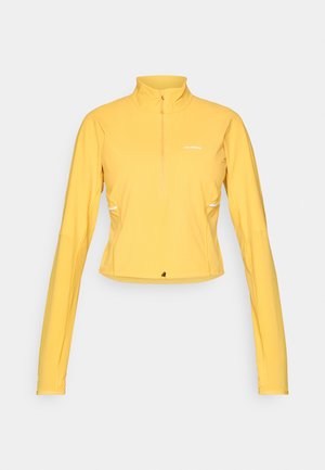 Camiseta amarilla de manga larga deportiva con cuello con media cremallera, ajuste ceñido, tejido ligero y detalle del logo en el pecho.