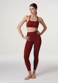 Top sportivo color bordeaux con spalline regolabili abbinato a leggings high-waisted aderenti dello stesso colore, caratterizzati da una texture liscia.