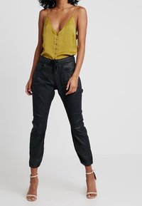 Gul silkekjolm med knappar som matchas med svarta tapered joggers, med fickor och elastiska manschetter, kompletterat med beige höga klackskor.