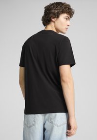 Sort bomulds t-shirt med korte ærmer og rund hals, med et enkelt design og afslappet pasform, set bagfra.