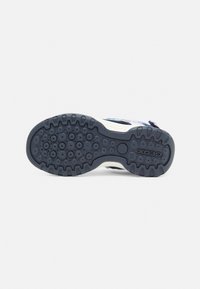 Suela de zapato en goma negra con patrones de tracción circulares, con una forma contorneada y la marca Geox. Diseñada para ofrecer agarre y durabilidad.