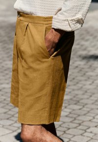 Tan linnedeture shorts med en afslappet pasform, som har sidelommer, knaplukning og diskrete læg. Stoffet har et blødt, tekstureret udseende.