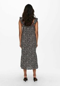 Vestido negro de flores con tirantes con volantes, de longitud media, con un corsé ajustado y una falda fluida, mostrado desde la parte de atrás. Zapatos de tacón visibles.
