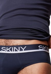 Marineblauwe ondergoed met een witte SKINY-logo op een elastische tailleband, met een gladde stoftextuur en een aangesloten ontwerp.