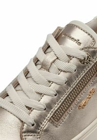 Baskets dorées métalliques avec des lacets blancs. Dotées d'une fermeture éclair décorative sur le côté et d'accents texturés. Matériau en cuir lisse et bout rond.