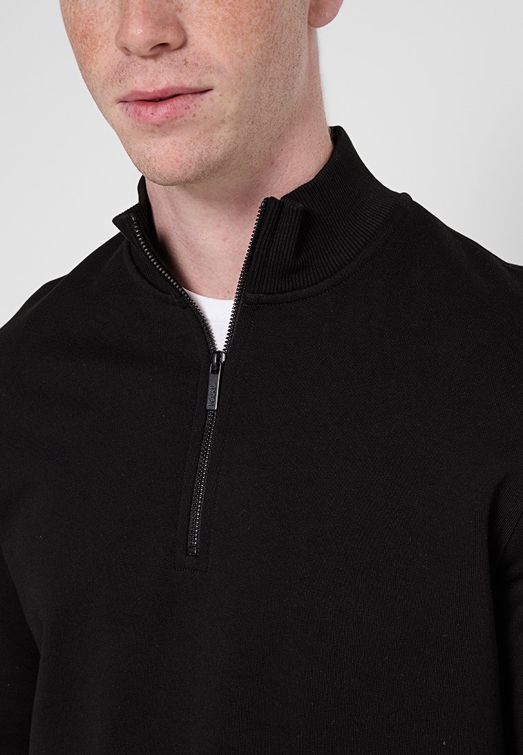 Schwarzer Reißverschluss-Pullover mit hohem Kragen, aus weichem Stoff, mit glatter Textur und einem subtilen Glanz am Reißverschluss.