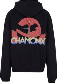 Fekete kapucnis felső, amelyen egy nagy grafika látható naplementével, hegyekkel és fákkal. A "CHAMONIX" felirat színátmenetes kék és sárga betűkkel jelenik meg.