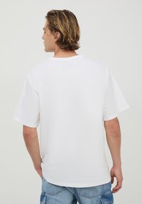 T-shirt bianco in cotone con scollatura rotonda e maniche corte. Presenta una vestibilità comoda e una parte posteriore semplice senza grafiche o elementi di design.