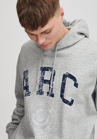 Hoodie gris avec grand imprimé bleu marine "ARC", capuche avec cordon de serrage et design graphique usé. Tissu doux avec poignets et ourlet côtelés.