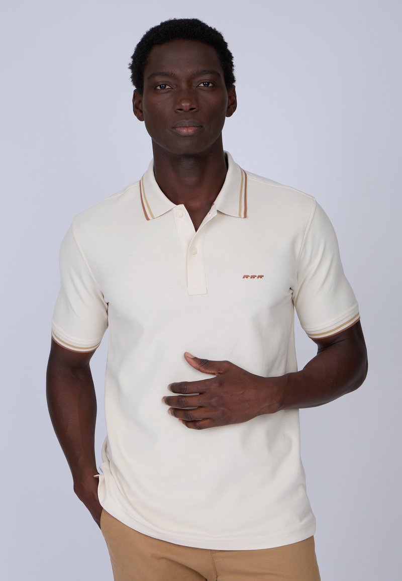 Polo beige avec col et manches rayés marron, fabriqué en tissu texturé. Présente un petit motif brodé sur la poitrine.