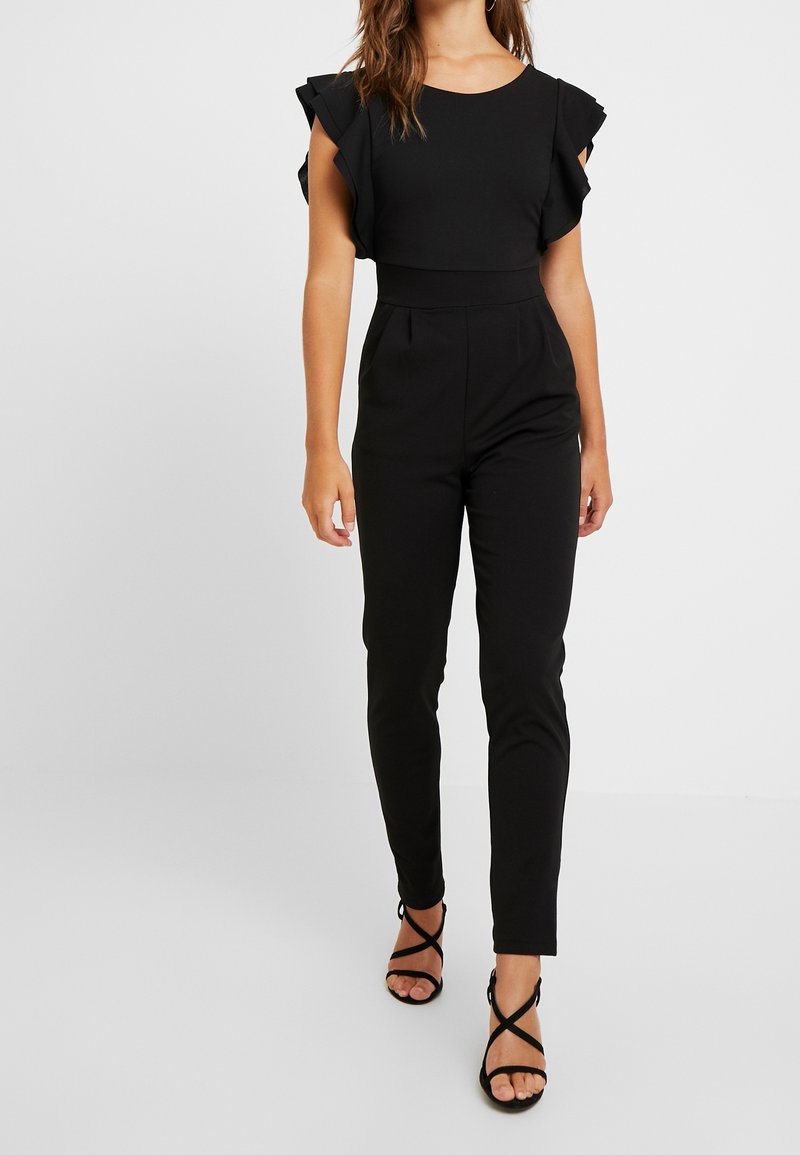 Svart jumpsuit med volangade korta ärmar, slim-fit ben och hög midja. Kombinerad med svarta remsandaler. Slät, töjbar tyg.