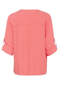 Camicia leggera di colore rosa corallo, con scollo rotondo, maniche a tre quarti e dettaglio a linguetta per arrotolare le maniche. Texture morbida, vestibilità comoda.