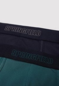 Två par herrunderkläder med elastiska midjeband. Det ena är mörk marinblå med grå text "SPRINGFIELD", det andra är teal med grön text.
