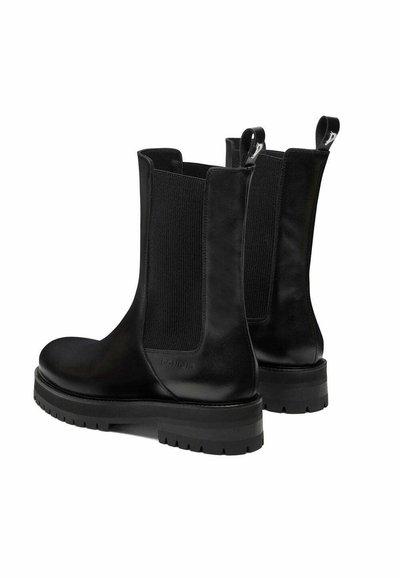 Bottines en cuir noir avec des panneaux latéraux élastiques, un bout rond et une semelle en caoutchouc robuste présentant un design de semelle texturée.