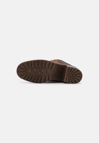Suela de zapato marrón con un patrón de relieve robusto y un tacón elevado, fabricada en goma duradera con textura visible y detalles de marca.