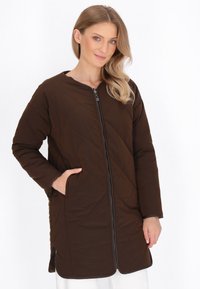 Cappotto lungo trapuntato marrone con zip frontale, colletto rotondo e tasche laterali. Presenta un'esterno liscio con un interno morbido e foderato.