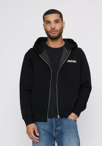 Melns zip-up kapucis ar kangaroo kabatu, pelēki akcenti un "CREATIVE DEPT." logo. Apvienots ar ziliem džinsiem. Mīksta auduma tekstūra.
