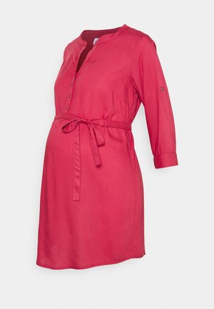 Vestido premamá rojo con mangas tres cuartos, cuello con botones y cinturón de lazo en la cintura sobre un fondo liso.