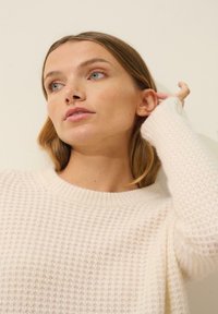 Kremowy sweter dziany o fakturze wafli, z ściągaczem przy dekolcie i długimi rękawami. Miękki, lekki materiał, zaprojektowany z myślą o komforcie.