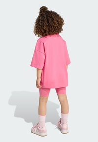 Lyserød oversized t-shirt, matchende lyserøde cykelshorts, hvide stribede sokker og lyserøde sneakers med hvide detaljer. Krøllet hår opsat.
