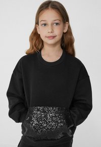 Czarna bluza z długim rękawem, z prążkowanym kołnierzem i cekinową czarną kieszonką na dole z przodu. Miękka faktura materiału.