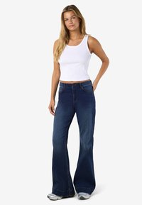 Baltas ribotas tankinis viršus derinamas su tamsiai mėlynais išplatintais džinsais. Džinsai turi klasikinį dizainą su priekinė kišene ir subtiliu siuvimo akcentu.