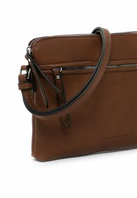 Bolso cruzado de cuero marrón con una correa negra, compartimentos con cremallera, una textura suave y detalle de marca en relieve en el lateral.