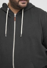 Felpa nera con zip in materiale cotone, dotata di coulisse bianca, zip argentata e tasca frontale. Design semplice con una vestibilità comoda.