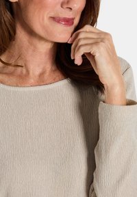 Beige strukturierter Langarm-Oberteil mit weitem Ausschnitt. Mit gerippter Oberfläche und weichem Stoff, der ein lässiges Design unterstreicht.