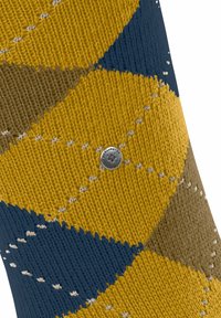 Il tessuto intrecciato presenta un motivo diagonale giallo, blu navy e marrone con piccole cuciture bianche, e un logo circolare argento al centro.