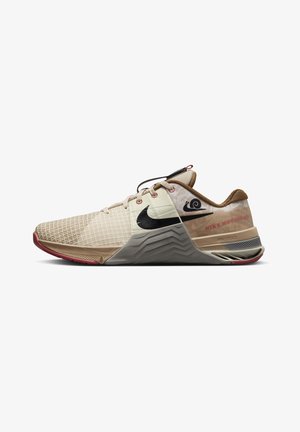 Beżowo-brązowe niskie buty Nike z czarnym logo, przednia część z wzorzystej siateczki, amortyzowana podeszwa i czerwone akcenty na spodzie i przeszyciach.