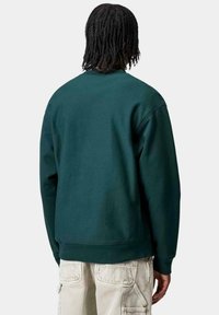Sudadera de color verde oscuro hecha de una tela suave, con cuello redondo y puños acanalados. La parte trasera presenta un diseño limpio sin logotipos ni patrones.