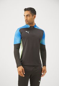 Schwarzes sportliches Quarter-Zip-Oberteil mit blauen und grünen Akzenten. Verfügt über ein texturiertes Muster an den Ärmeln und ein reflektierendes Logo auf der Brust.