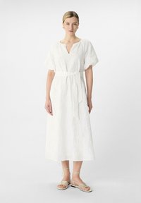 Weißes besticktes Kleid mit V-Ausschnitt und kurzen Puffärmeln, tailliert mit einem passenden Gürtel. Tragen mit beigen Riemchensandalen.