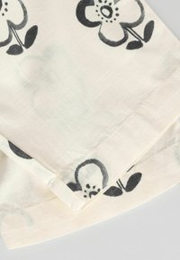 Blumenerstoff mit einem hellen cremefarbenen Hintergrund, der mit schwarzen Blumenmotiven und grünen Akzenten verziert ist. Das Material ist leicht und strukturiert.