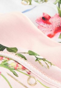 Capas de tela con estampado floral en suave rosa y blanco, con delicadas costuras y un detalle circular dorado.