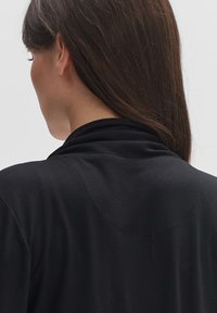 Zwarte, aansluitende top met een zachte textuur en een opgerolde kraag. Heeft een eenvoudig ontwerp met minimale stikdetails op de schouders.