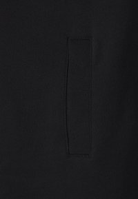 Svart sweatshirttyg med en diskret sidficka och rena sömmar. Texturen är jämn med en enhetlig yta.