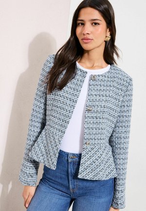 Hellblauer Tweed-Blazer mit Peplum-Design, rundem Ausschnitt und silbernen Knopfverschlüssen. Getragen über einem weißen Oberteil und Jeans.