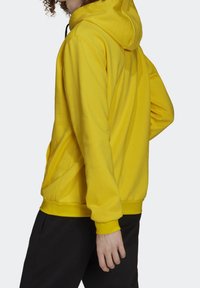 Geel hoodie van zacht materiaal, met een trekkoordcapuchon, lange mouwen en een relaxte pasvorm. Zijzak zichtbaar aan de linkerkant.