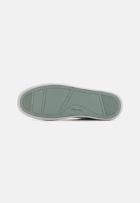 Suola di scarpa in gomma verde con motivi testurizzati, caratterizzata da sezioni segmentate e un bordo bianco. Testo del marchio "Calvin Klein" impresso sulla superficie.