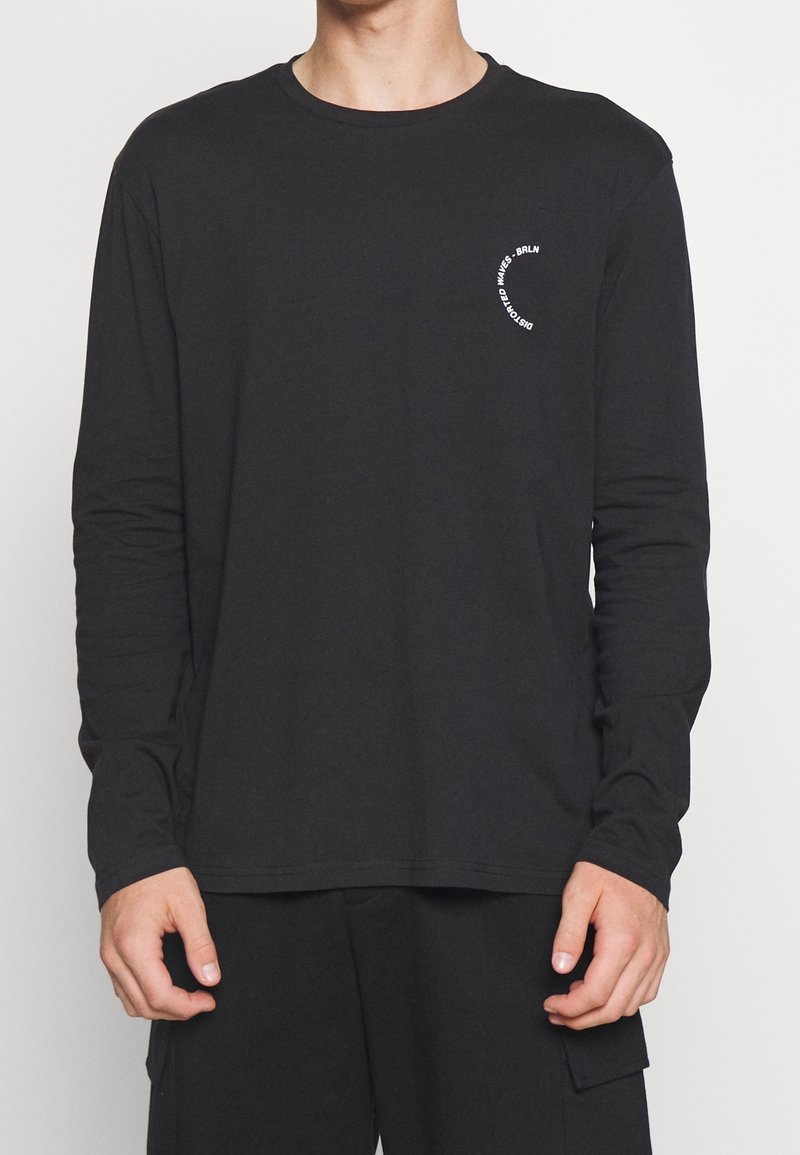 Langärmliges schwarzes T-Shirt aus weicher Baumwolle mit rundem Halsausschnitt und einem weißen runden Logo, das auf der Brust aufgedruckt ist.
