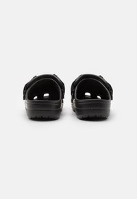 Black sandals with open back, adjustable strap, textured sole, and ventilation holes, featuring a smooth plastic finish.