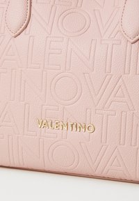 Torba iz teksturirane roza usnje z embosiranim logotipom in zlatimi detajli. Gladki poudarki dopolnjujejo dizajn.