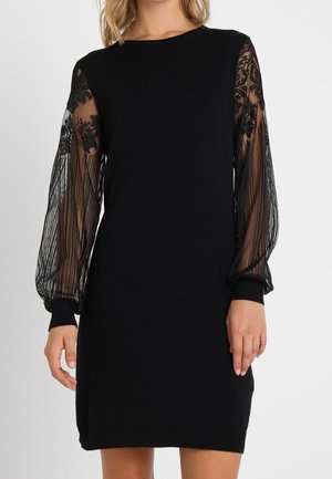 Czarna sukienka do kolan z przezroczystymi długimi rękawami zdobionymi kwiatową koronką i pionowymi paskami, dopasowane mankiety oraz okrągły dekolt.