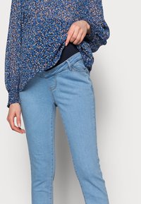 Ljusblå skinny jeans med en slät yta, med medelhög midja och subtila sömnadsdetaljer, matchade med en flödande blommig blus.