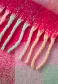 Écharpe douce en laine avec extrémités à franges, dans des nuances de rouge, rose, vert et pêche, montrant des fibres texturées et un mélange de couleurs.