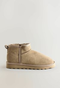 Botas de tobillo de ante en color marrón con punta redonda y superficie texturizada. Presenta un caña corta, panel lateral elástico y una suela plana de goma.